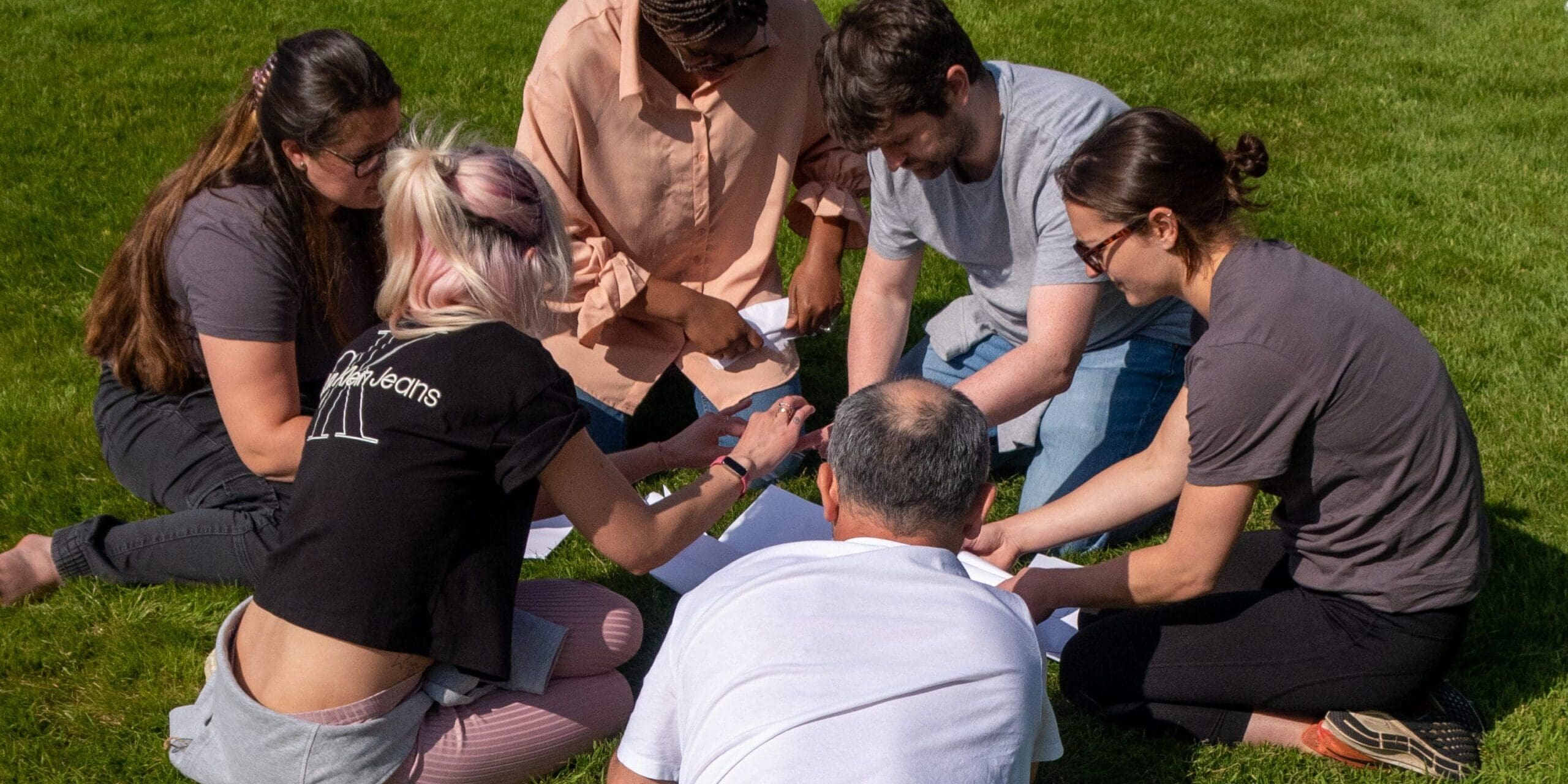 A team of Hyphen8 staff are sat on the grass on a sunny day doing a team building exercise.