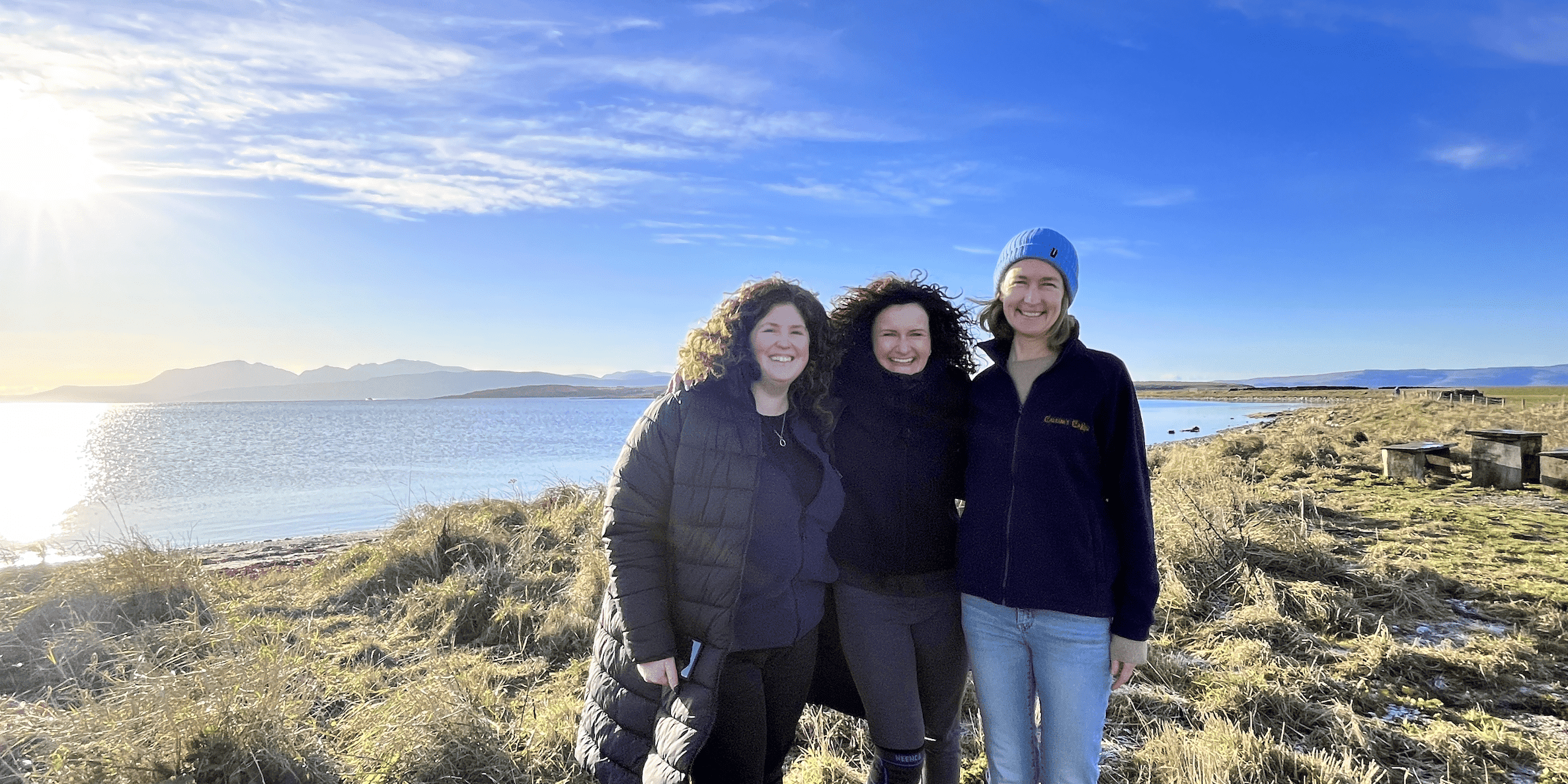 Three women stand together smiling, on a crisp wintery day.