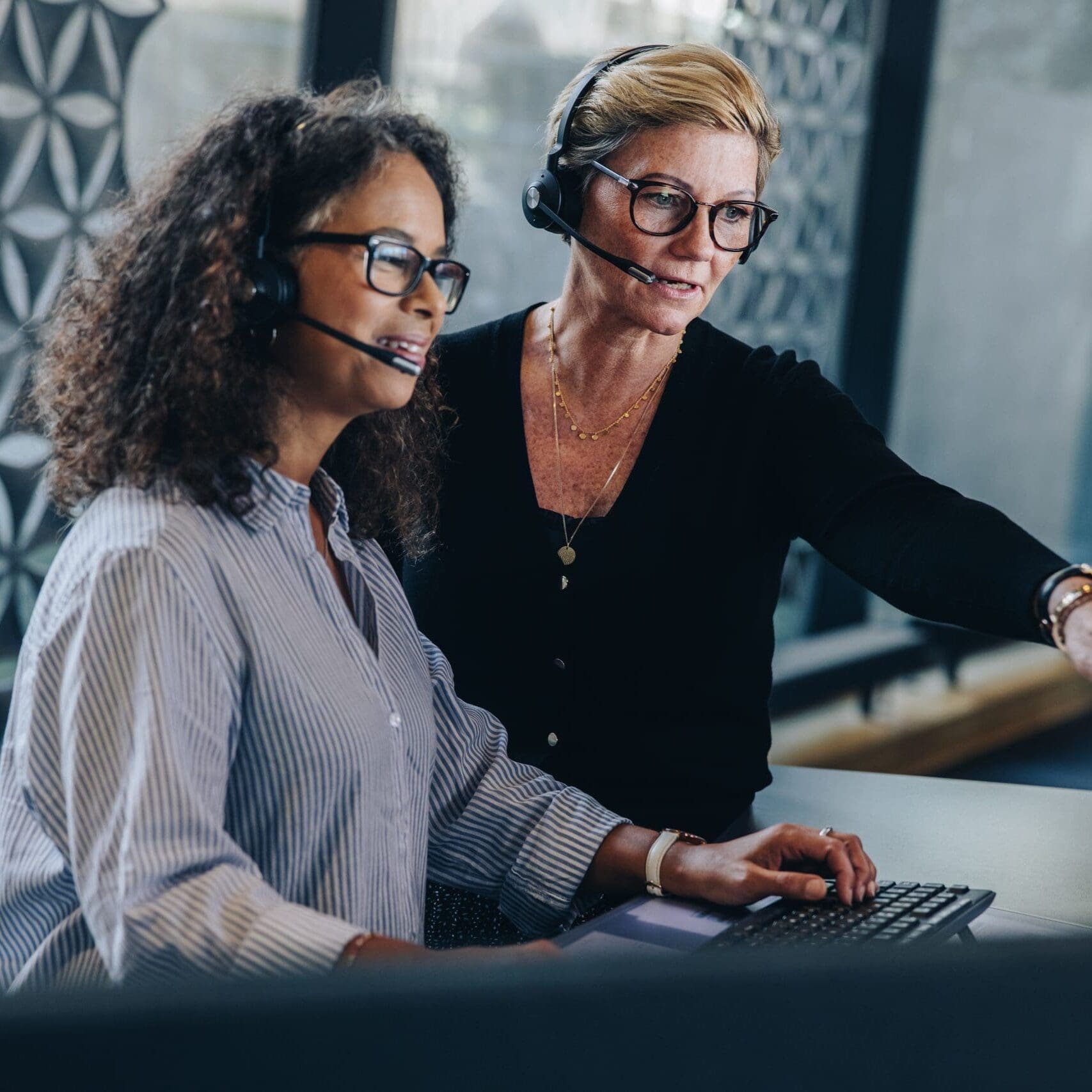Two,Businesswomen,Wearing,Headset,Working,Together,On,Computer,In,Call