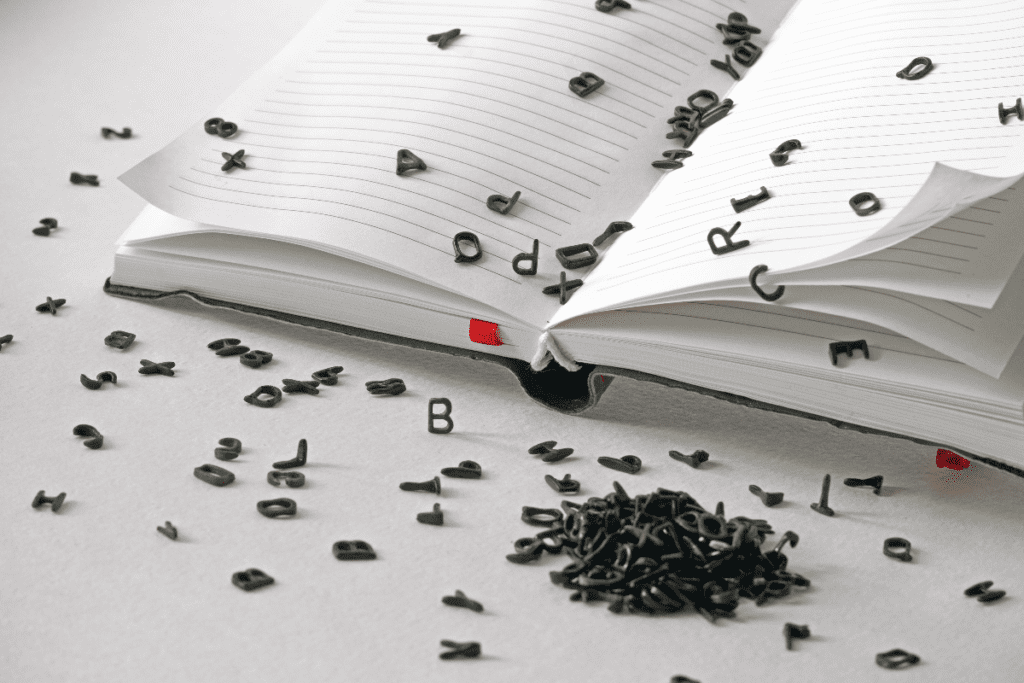 Black letters pour out from blank pages of a book on a white table, education and dyslexia concept