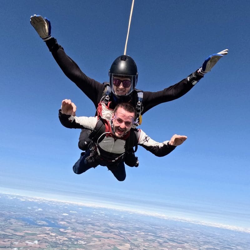 Garry is skydiving through the sky with another man, you can see the land and it's curvature below.