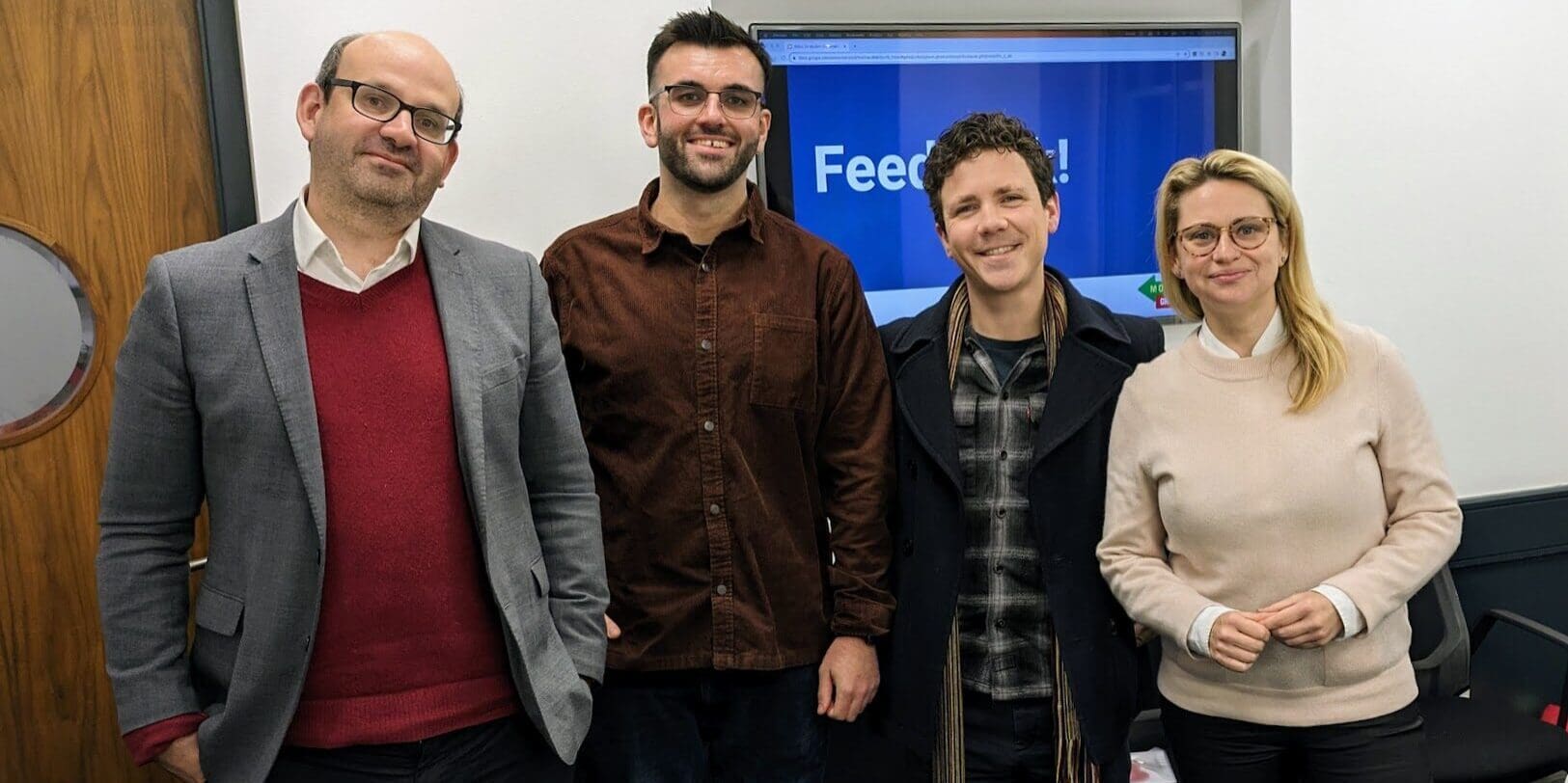 Four people stand and smile at the camera in a training room.