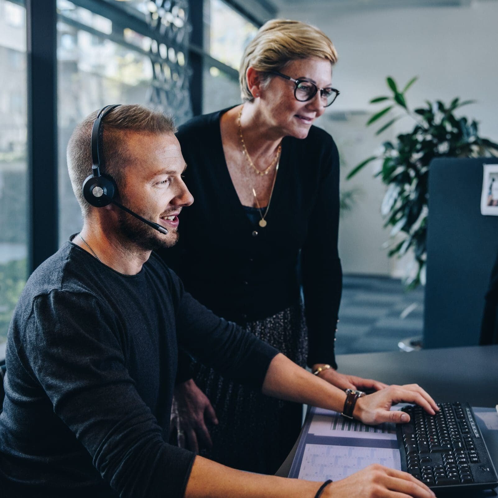 Senior,Manager,Standing,By,Young,Man,Wearing,Headset,Working,On